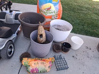 Sale Photo Thumbnail #113: Assorted lawn and garden supply lot including WAGNER'S Songbird Supreme Wild Bird Food, potting mix, multiple plastic and ceramic planters/pots, woven decorative bird roosts/nests, and a suet cage feeder. Items show signs of previous outdoor use and soil 