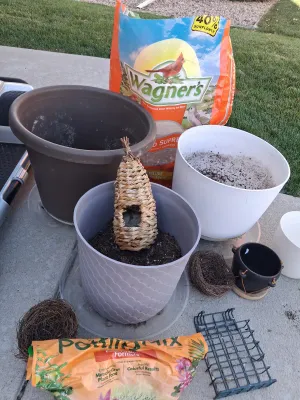 Sale Photo Thumbnail #115: Assorted lawn and garden supply lot including WAGNER'S Songbird Supreme Wild Bird Food, potting mix, multiple plastic and ceramic planters/pots, woven decorative bird roosts/nests, and a suet cage feeder. Items show signs of previous outdoor use and soil 