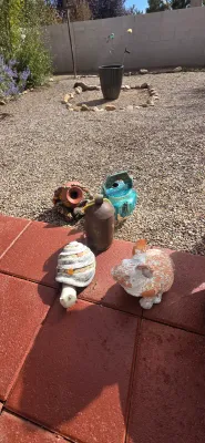 Sale Photo Thumbnail #9: Collection of outdoor garden decor including ceramic animal statues, a metal cowbell, and decorative pots on a gravel patio.