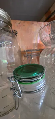 Sale Photo Thumbnail #49: Collection of glass glassware and jars, including a small wire-bail jar with a green glass lid and a large graduated glass jar.