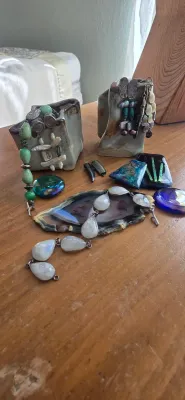 Sale Photo Thumbnail #18: Collection of artisan jewelry and mineral specimens including a teardrop moonstone-style necklace, turquoise beaded bracelet, wire-wrapped earrings, glass cabochons, and an agate slice on a wooden surface.