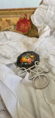 Sale Photo Thumbnail #12: Vintage brooches including a silver bicycle-shaped pin and a hand-painted floral Zhostovo-style lacquered pin, displayed on white lace fabric.