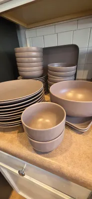 Sale Photo Thumbnail #5: Modern matte mauve ceramic dinnerware set including stacks of plates, bowls, and serving trays.