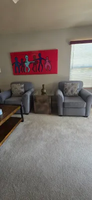 Sale Photo Thumbnail #6: Pair of contemporary gray upholstered armchairs paired with patterned throw pillows and a glass-top accent end table.