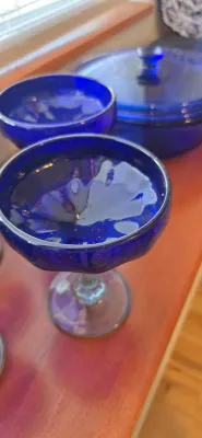 Sale Photo Thumbnail #19: Cobalt blue glass stemware piece alongside matching glassware including a covered casserole dish, all displayed on a wooden surface.