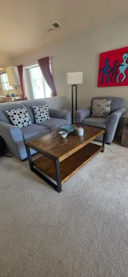 Sale Photo Thumbnail #4: Rustic industrial wooden coffee table with black metal frame, set alongside a gray upholstered loveseat and matching armchair.