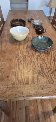 Sale Photo Thumbnail #3: Rustic wooden dining table featuring various ceramic items including a yellow mixing bowl, green pottery dish, and small brown teapot.
