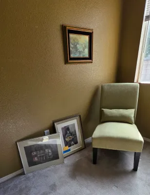 Sale Photo Thumbnail #27: Contemporary armless accent chair upholstered in sage green fabric alongside three framed artwork pieces displayed on the wall and floor.