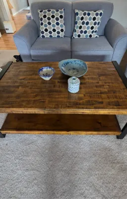 Sale Photo Thumbnail #24: Rustic wood and black metal coffee table with lower shelf, paired with decorative pottery bowls and a jar, positioned in front of a gray upholstered loveseat.