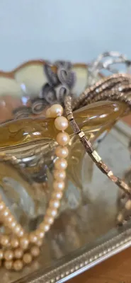 Sale Photo Thumbnail #13: Vintage pearl strand necklace resting alongside other costume jewelry inside a ruffled amber glass dish on a silver-plated tray.