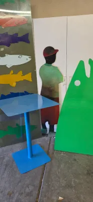 Sale Photo Thumbnail #50: Blue painted metal pedestal table displayed alongside colorful metal cutout artwork, including fish shapes and a human figure silhouette.