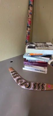 Sale Photo Thumbnail #25: Australian Aboriginal dot-painted wooden boomerang accompanied by a stack of assorted books and a tall carved wooden totem pole.