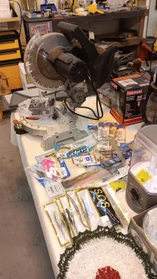 Sale Photo Thumbnail #31: A benchtop compound miter saw displayed alongside an assortment of fishing gear, lures, and household items on a table.