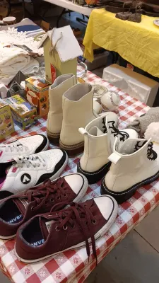 Sale Photo Thumbnail #37: Collection of women's shoes displayed on a red gingham tablecloth, including maroon Converse sneakers, white lace-up boots, cream slip-on ankle boots, and athletic sneakers.