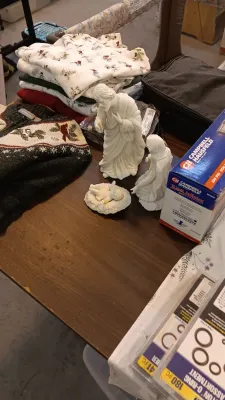 Sale Photo Thumbnail #44: A collection of household items including folded winter sweaters, a white porcelain nativity set, and a boxed Campbell Hausfeld tire inflator on a wooden table.