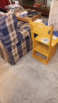 Sale Photo Thumbnail #58: Yellow-stained wooden folding step stool chair sitting next to a plaid upholstered armchair and a coffee table filled with household items.