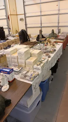 Sale Photo Thumbnail #53: Tables loaded with estate sale items, including stacks of boxed Danbury Mint Corvette die-cast models, religious figurines, small decor, and collectibles.