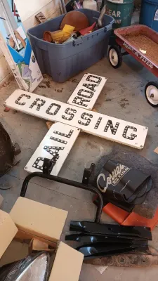 Sale Photo Thumbnail #57: Vintage reflectorized Railroad Crossing crossbuck sign lying on a garage floor alongside Corvette accessories, lawnmower blades, and a red Radio Flyer wagon.