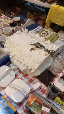 Sale Photo Thumbnail #36: Collection of household items including embroidered and lace linens, white coffee mugs, Eero Wi-Fi routers with power adapters, and various small decor objects on a red gingham tablecloth.