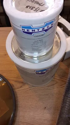 Sale Photo Thumbnail #54: Stacked metal cans of Hentzen industrial curing agent and primer sitting on a wooden surface.