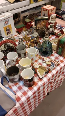 Sale Photo Thumbnail #33: Collection of holiday decor and ceramic mugs arranged on a red-and-white checkered tablecloth, including Santa figurines, Christmas tins, and ornaments.