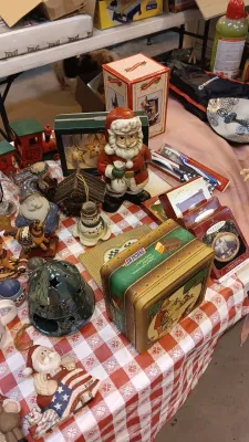 Sale Photo Thumbnail #32: Collection of holiday decor and collectibles including Hallmark Keepsake ornaments, a vintage Snickers tin, and Santa figurines, displayed on a red and white checkered tablecloth.
