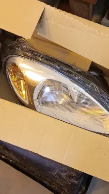 Sale Photo Thumbnail #65: Automotive headlight assembly wrapped in protective plastic inside a cardboard box.