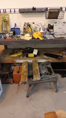 Sale Photo Thumbnail #15: Workshop workbench filled with various tools, automotive fluids, hardware, and a portable folding workmate table in the foreground.