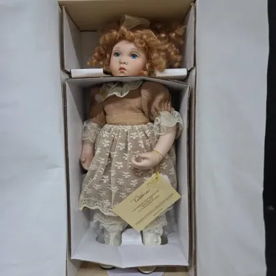 Victoria porcelain collector doll with curly blonde hair and a lace-trimmed dress, stored in its original box with attached tag.