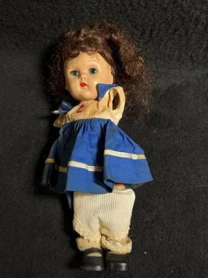 Vintage mid-century small storybook style doll with brown curly hair, blue dress, and painted facial features. Shows signs of wear and...