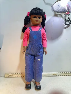 Vintage large-scale doll featuring dark hair in pigtails, wearing blue denim overalls over a pink long-sleeved shirt and black shoes.