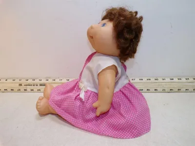 Vintage Cabbage Patch Kids doll with brown curly yarn hair, blue eyes, and a pink polka dot dress.