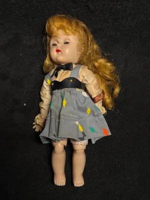 Vintage hard plastic storybook-style doll with wavy strawberry blonde hair, wearing a grey patterned jumper over a beige blouse.