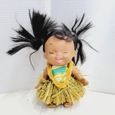 Vintage Hawaiian hula girl doll featuring pigtails, a straw grass skirt, and a yellow lei.