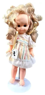 Vintage plastic doll with curly blonde hair, wearing a striped dress and displayed on a metal doll stand.