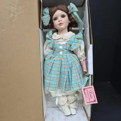 Collectible porcelain doll named "Lois" from the Florence Maranuk Collection, featuring brown hair, hair bows, and a blue plaid...