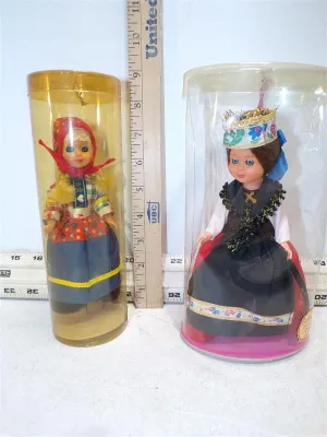 Pair of vintage souvenir dolls dressed in detailed European traditional folk costumes, housed inside clear plastic cylinder containers.