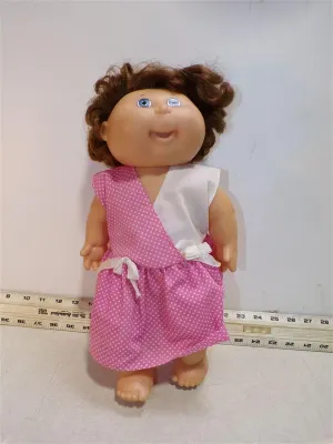Vintage 1980s Cabbage Patch Kids doll with short curly brown hair and blue eyes, wearing a pink polka dot and white dress.
