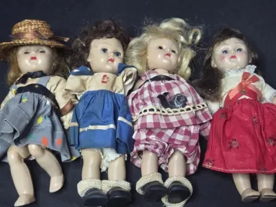 Collection of four vintage hard plastic storybook dolls with sleep eyes and fabric dresses, circa mid-20th century.