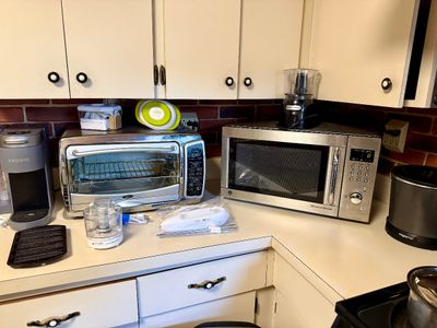 Collection of small kitchen appliances, including a stainless steel GE microwave, an Oster toaster oven, a grey Keurig coffee maker, and...