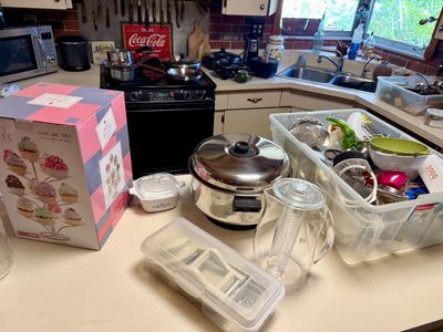 Collection of kitchen items including a boxed cupcake tree, stainless steel cookware, CorningWare dish, glass infuser pitcher, and...