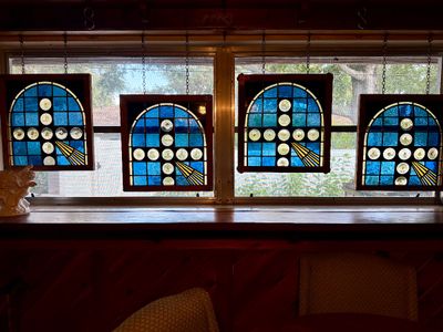 Set of four framed stained glass window panels featuring blue and clear roundel cross motifs, suspended by hanging chains.