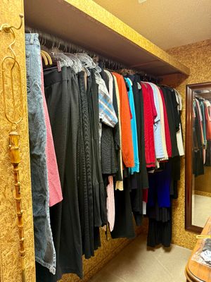A collection of women's clothing, including denim, pants, sweaters, and shirts, organized on hangers in a closet.