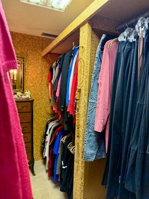 Walk-in closet filled with vintage women's clothing hanging on racks, including sweaters, pants, and dresses.