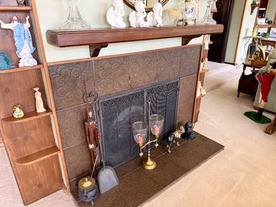 Wooden fireplace surround with patterned brown tile, wrought iron mesh screen, brass candle holder, and various decorative hearth...