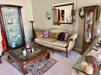 Formal living room set featuring a French provincial style sofa, glass-top wooden coffee table, dark wood curio cabinets displaying...