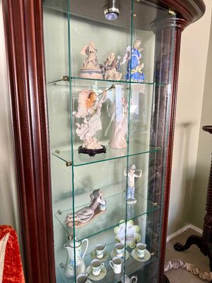 Traditional cherry wood display cabinet filled with porcelain figurines, angel statues, and fine china teacups and saucers.