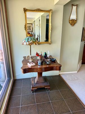Antique tilt-top pedestal table displaying a leaded glass Tiffany-style table lamp and various decorative accents beneath a gilded wall...