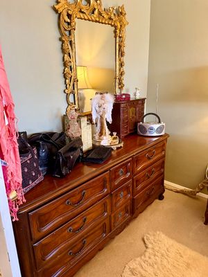 French Provincial style long wooden dresser topped with handbags, an ornate gilt framed mirror, and decorative accessories.
