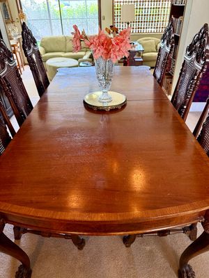 Traditional mahogany extension dining table set with intricate ornate carved high-back chairs and ball-and-claw feet.